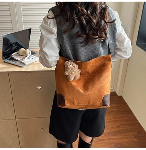 Détail d'un cabas en daim marron avec breloque ours en peluche et coins en cuir foncé