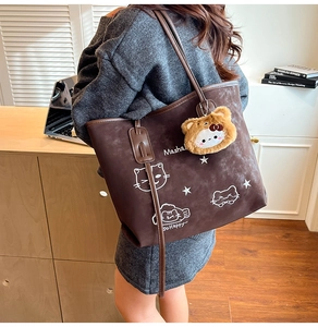 Detail of dark brown suede tote bag with cat illustration and plush charm on strap