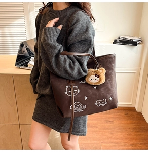 Detail of dark brown tote bag with cute cat print and plush bear charm on model