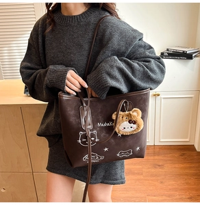 Detail of a brown suede tote bag featuring a cute cat print and a plush bear charm