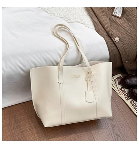 Close-up of cream faux leather tote bag with gold logo lettering and fine stitching