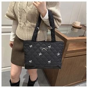 Detail van zwarte gewatteerde shopper met witte strikborduursels en lederen bodem op model