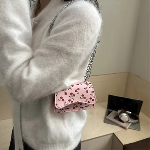 Pink mini crossbody bag with cherry prints and silver chain strap shown on model
