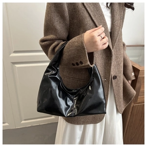 Detail of glossy black patent leather handbag with a minimalist crescent silhouette