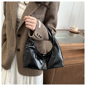 Detail of a black glossy patent leather hobo shoulder bag with a sleek crescent shape