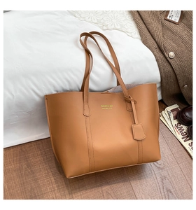 Detailed top view of a tan leather tote bag with long straps on minimalist bedding decor