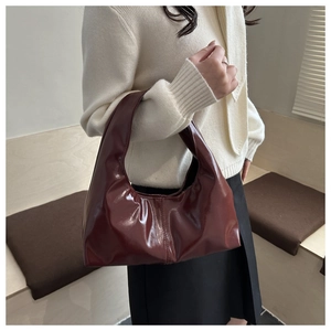 Close-up of a burgundy patent leather hobo bag worn by a model in a knit sweater