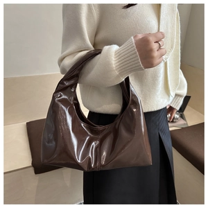 Detail of dark brown glossy patent leather shoulder bag with seamless handle design