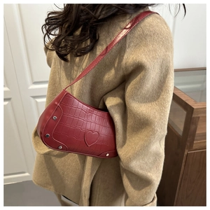 Detail of red croc-effect underarm bag with heart patch and metal rivets worn on the shoulder