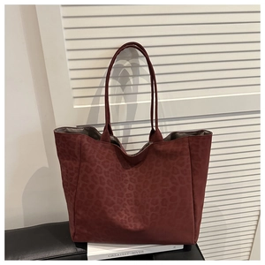 Gros plan sur le motif léopard gaufré du sac cabas en daim bordeaux avec bandoulière