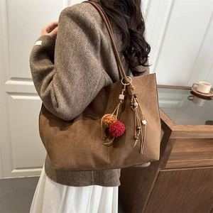 Brown faux suede tote bag with bohemian tassel charm shown from a side-view angle