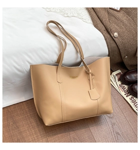 Close-up of beige leather tote bag with gold logo and long shoulder straps on wooden floor