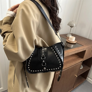 Retro black leather crescent bag with silver rivets shown on a shoulder in a home setting