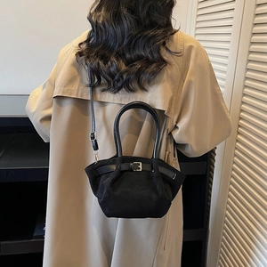 Chic black suede crossbody bag with gold hardware and top handle shown on a beige coat
