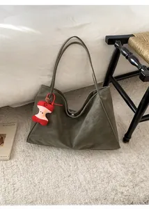 Borsa tote verde oliva opaca con ciondolo a mela rossa posata su un tappeto beige