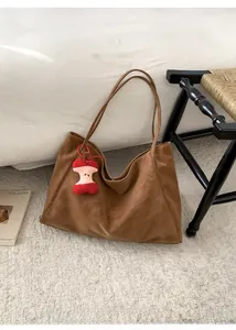 Dettaglio di una borsa tote in pelle scamosciata marrone con ciondolo a forma di mela