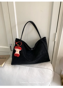 Dettaglio di una borsa tote nera capiente con un ciondolo creativo a forma di mela rossa