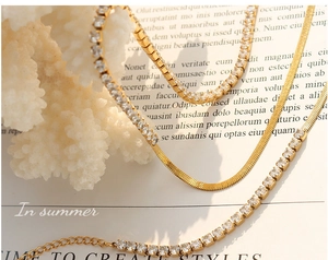 Detail of layered gold snake chain and sparkling zircon tennis necklace on coral stone
