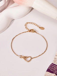 Dettaglio del bracciale con cuore a infinito dorato e zirconi bianchi su sfondo bianco