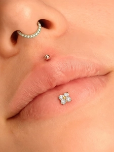 Detailed close-up of crescent moon septum ring and floral labret piercing with zircon stones