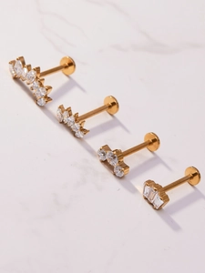 Detailed view of four gold labret studs with cubic zirconia on marble surface
