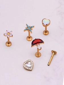 Detail of gold piercing set with star, heart, and mushroom charms on marble background