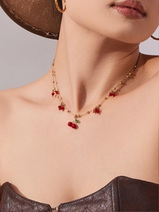 Dettaglio macro della collana con pendente a ciliegia placcata oro e perline rosse