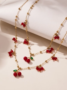 Dettaglio della collana con ciondolo a ciliegia dorata, cristalli rossi e foglie verdi