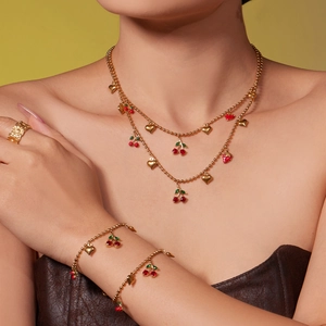 Parure de bijoux dorés avec pendentifs cerise et fraise sur fond chaud