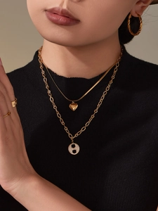 Détail de colliers dorés superposés avec pendentifs cœur et zircon sur col roulé noir
