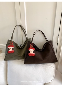 Dettaglio di grandi borse tote verde oliva e marroni con graziosi ciondoli a forma di mela
