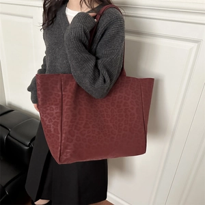Grand sac cabas bordeaux en daim à motif léopard pour femme porté à l'épaule par un mannequin