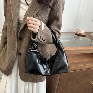 Minimalist black patent leather crescent handbag with glossy finish and metal buckles