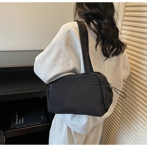 Detail of a black nylon shoulder bag showing a waterproof texture and side drawstring design