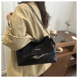 Detail of minimalist black leather tote bag featuring chain strap and fashion text logo