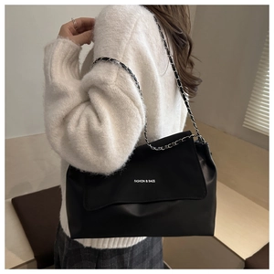 Detail of black leather tote bag featuring white fashion text and chain shoulder strap