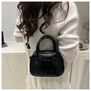 Close-up of a black textured mini crossbody bag featuring a gold zipper and twin handles