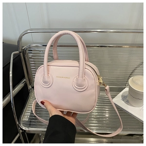 Close-up of pink round crossbody bag with fashion text detail and double top handles
