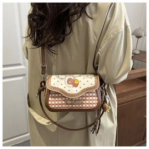 Detail of a plaid crossbody bag with bow decoration and cute brown bear charm
