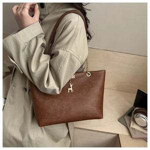 Detail of deep brown tote bag with gold deer charm and chain strap shown on a model