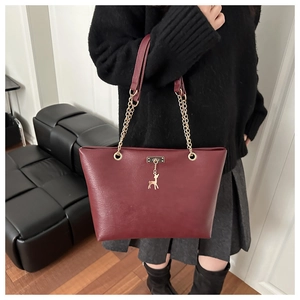 Close-up of wine red tote bag featuring gold deer charm and chain-link strap detail