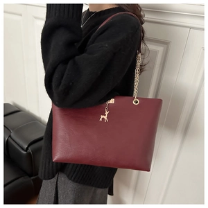 Détail d'un sac cabas bordeaux avec chaîne dorée et pendentif cerf sur un modèle