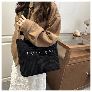 Close-up of black corduroy tote bag with white TOTE BAG embroidery and soft wide strap