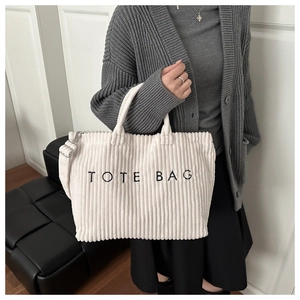Detail of white corduroy tote bag showing embroidered text and striped fabric texture