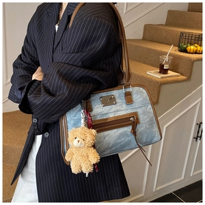 Détail du sac cabas en denim vintage avec bordure en cuir marron et breloque ours en peluche
