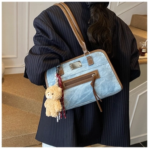 Detail view of denim tote bag featuring brown leather trim and a cute plush bear charm