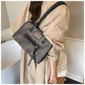 Detail of dark gray tote bag with long straps and front zipper pocket on model shoulder