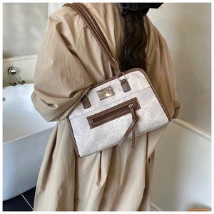 Detail of a contrast canvas tote bag with brown leather trim worn by a model