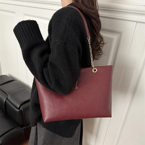 Burgundy textured leather tote bag with gold deer ornament and chain strap shown on model