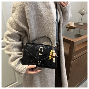 Detail of black crocodile texture handbag with gold buckle and beaded tassel charm